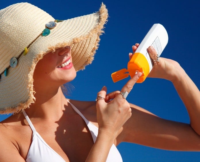 woman in hat applying sunscreen against a blue sky