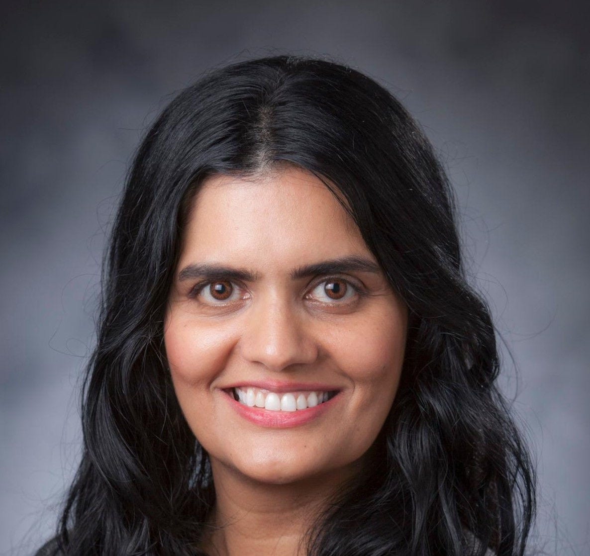 woman with long black hair wearing gray jacket over red scoop neck blouse