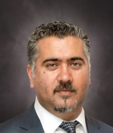 man with salt-and-pepper hair and mustache with small beard, checkered gray tie on white shirt
