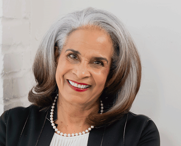 Smiling woman with gray hair wearing a black blazer and pearls